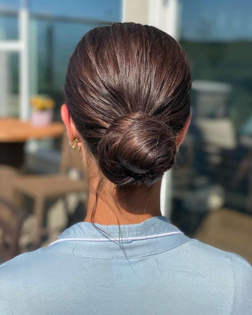 Dark brown hair styled into a sleek and smooth low bun at the nape.