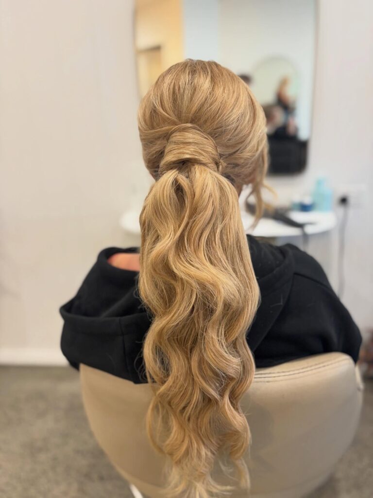 Long wavy blonde hair in a low ponytail with a wrapped section around the base.