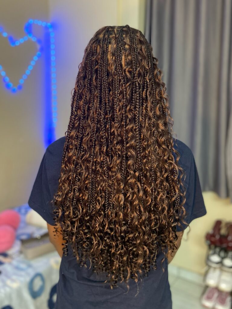 A back view of long knotless braids in dark brown and honey blonde featuring voluminous loose curls throughout the length.