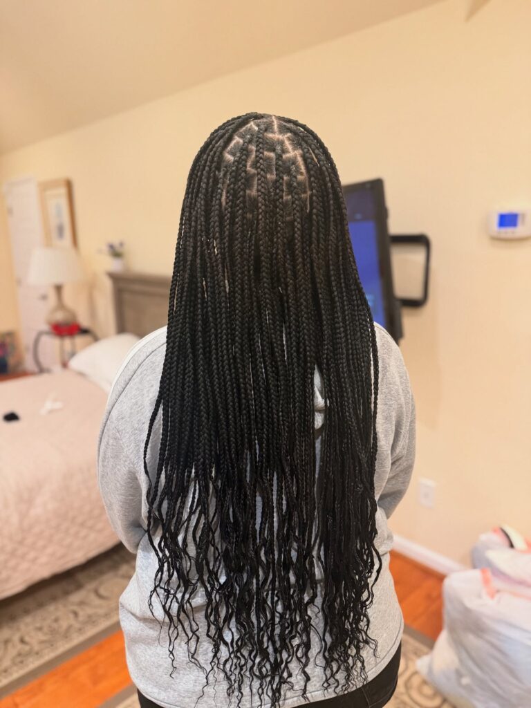 A woman stands with her back to the camera showcasing long black knotless braids with wavy curly ends reaching her lower back.