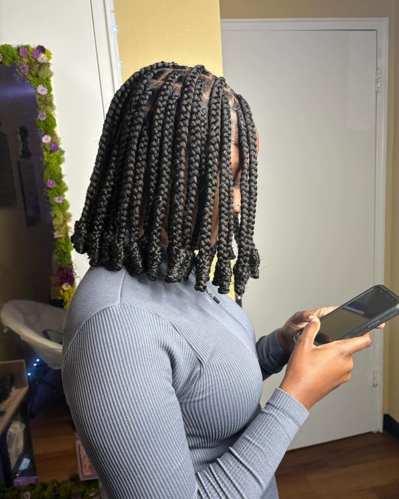 A side view of a person wearing shoulder length black box braids with thick sections and neatly curled ends.