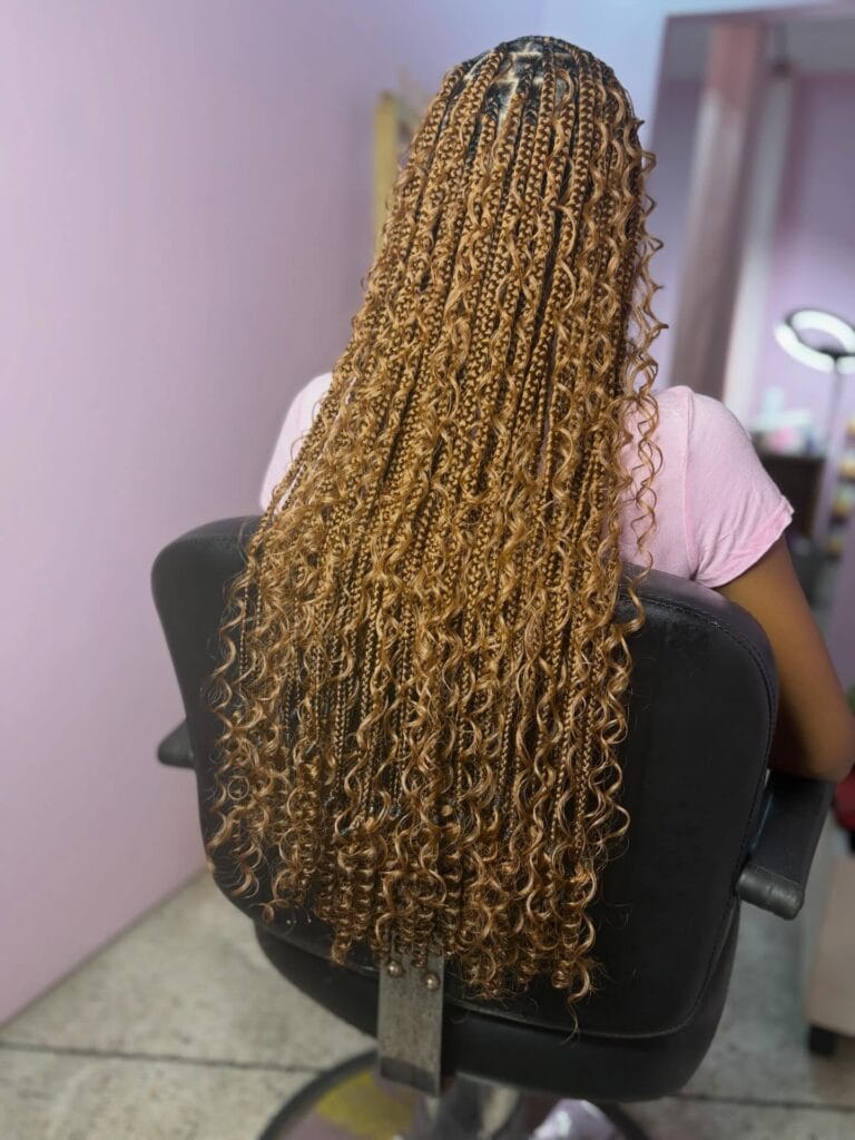 A back view of a woman sitting in a chair with long honey blonde box braids featuring tight curls throughout.