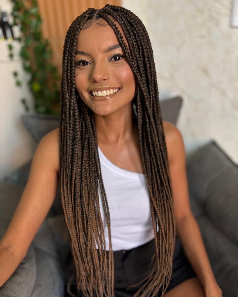 A smiling woman wearing long slim box braids in a warm chocolate brown color with a middle part.
