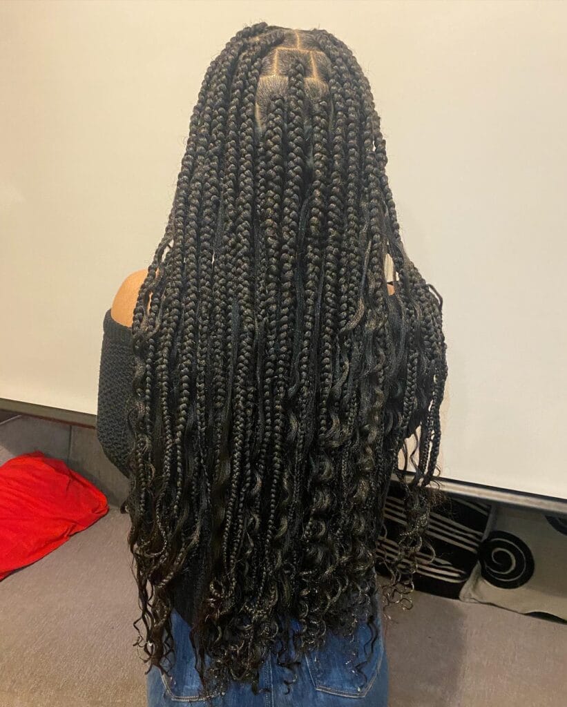 A back view of a woman with long black box braids blended with loose wavy hair extensions for a voluminous bohemian look.
