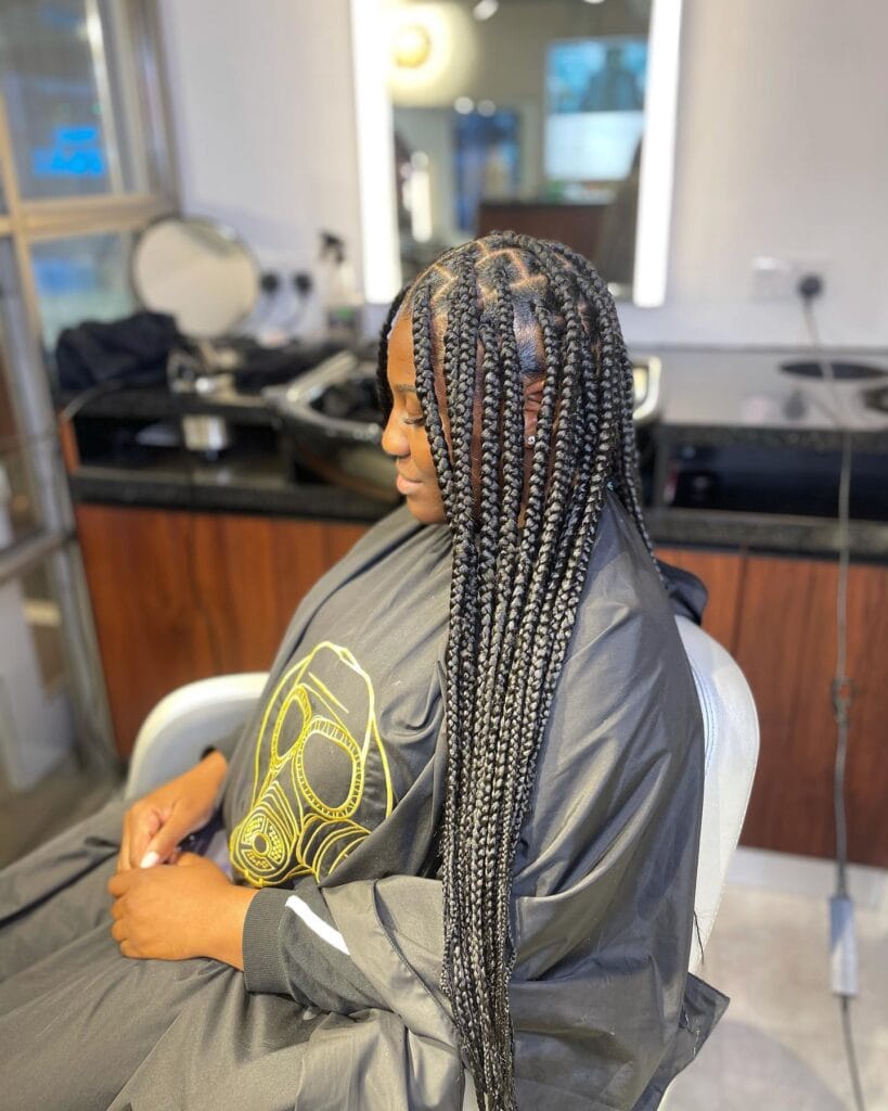 A side view of a person wearing long black box braids with sharp triangle sections at the scalp.