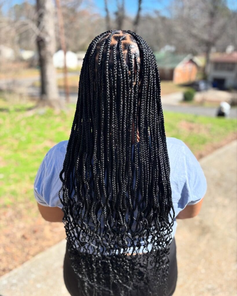 A back view of a woman outdoors wearing sleek black box braids that end in soft wispy curls.