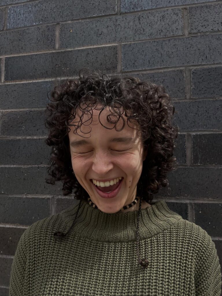 A laughing woman with a chin-length dark brunette curly bob featuring soft curly bangs.