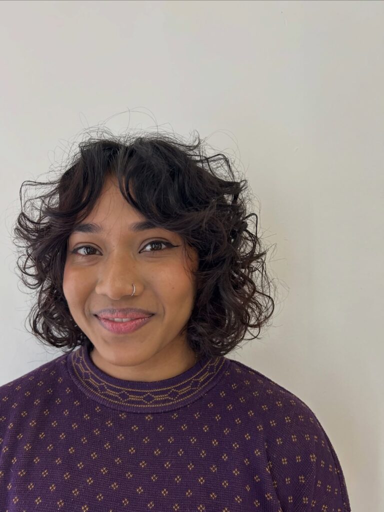 A smiling woman with a neck-length espresso-brunette curly bob featuring soft curtain bangs.