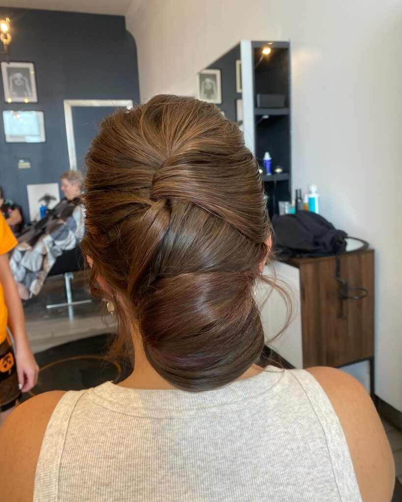 A woman viewed from the back, showing a medium brown low chignon with elegant, overlapping twisted layers.