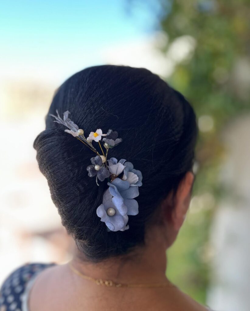 A woman viewed from the back is wearing a sleek black French twist updo decorated with blue and white floral hairpins.