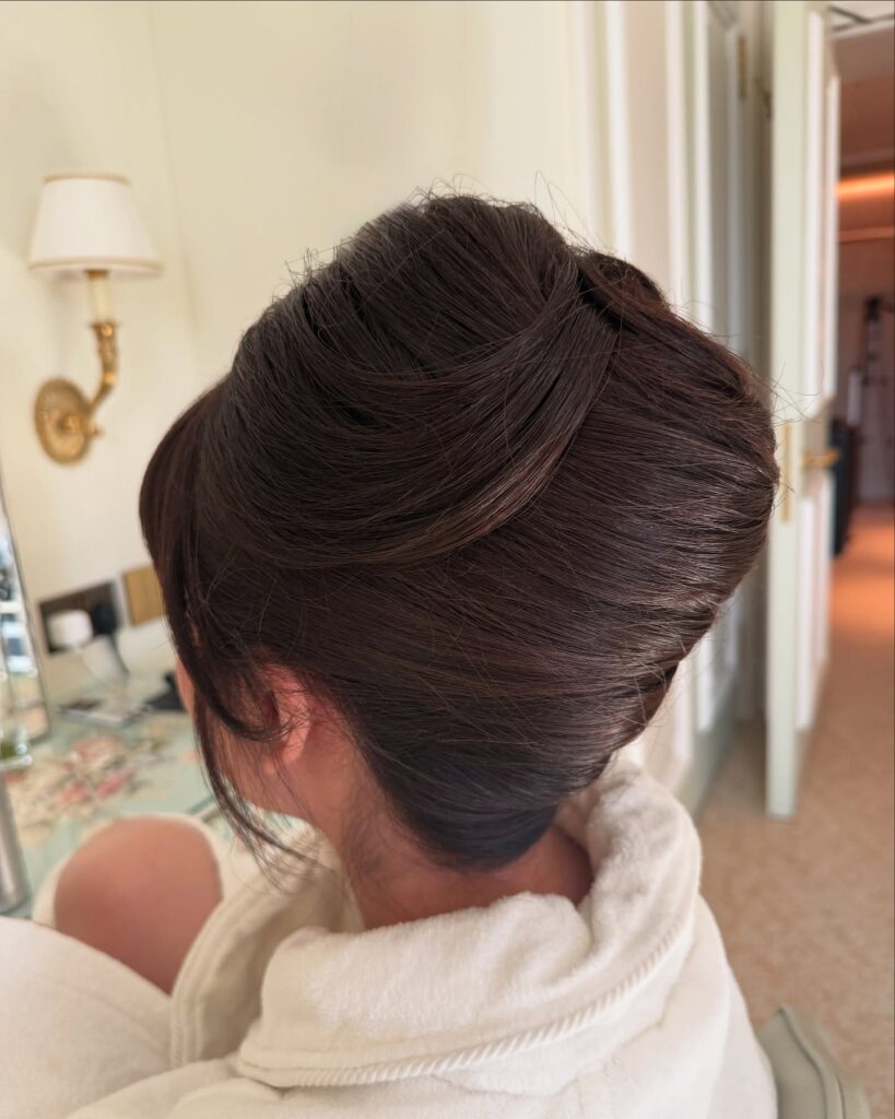 A woman seen from the back wearing a high-volume dark brunette beehive updo with smooth architectural layers.