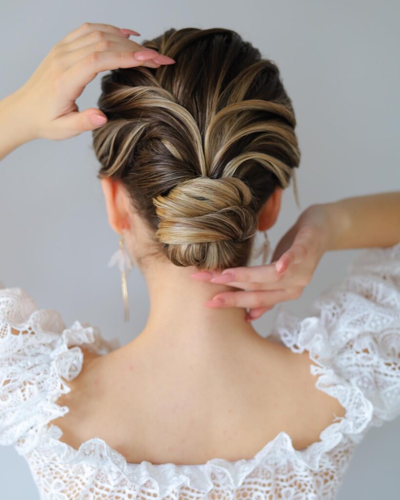 A detailed low bun hairstyle featuring sculptural ribbed sections and blonde highlights seen from the back.