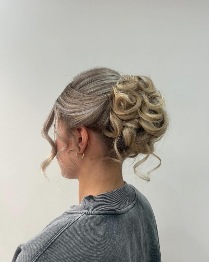 A side view of a cool ash blonde updo with polished sides and a voluminous cluster of curly rosettes at the back.