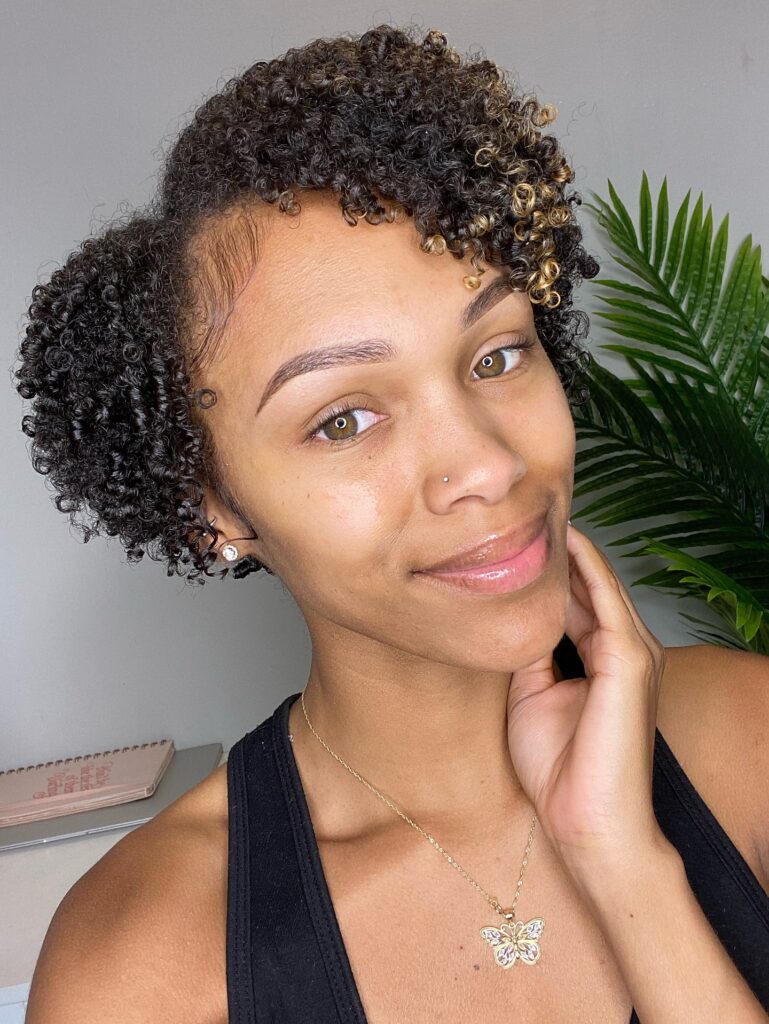 A woman with short, cropped dark curls featuring a few golden highlights and sleekly styled edges.