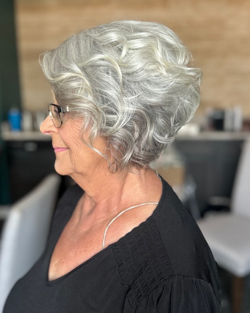 A profile view of a woman with a voluminous stacked bob in a shimmering silver color with soft sculpted waves.