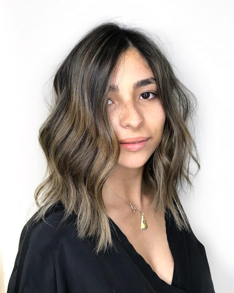 A person with a shoulder-length, sun-kissed wavy lob hairstyle and natural makeup.