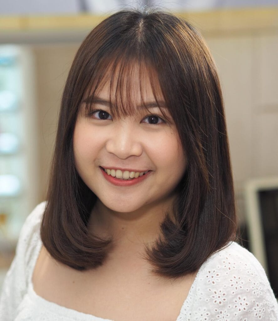 A smiling woman with a medium-length espresso brown haircut featuring wispy bangs and ends curled inward.
