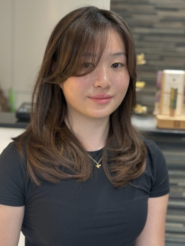 A young woman with a medium-length chestnut brown haircut featuring soft curtain bangs and layered ends.