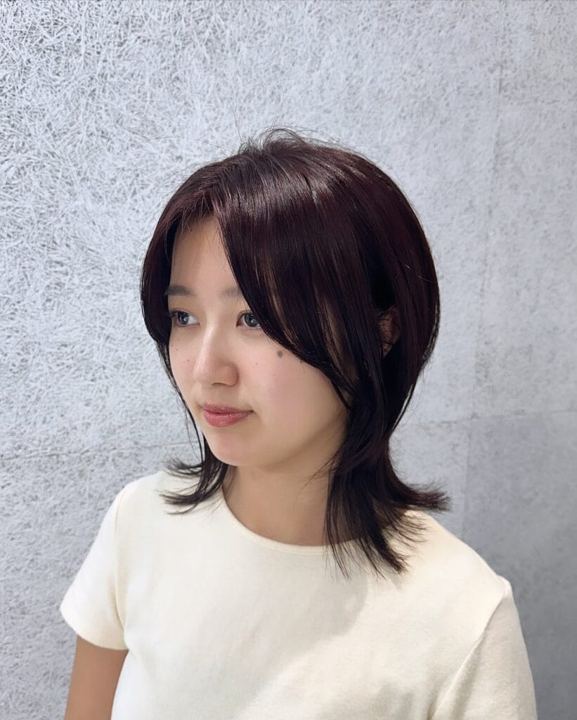 A woman with a medium-length deep plum shag haircut featuring flicked-out ends and face-framing layers.