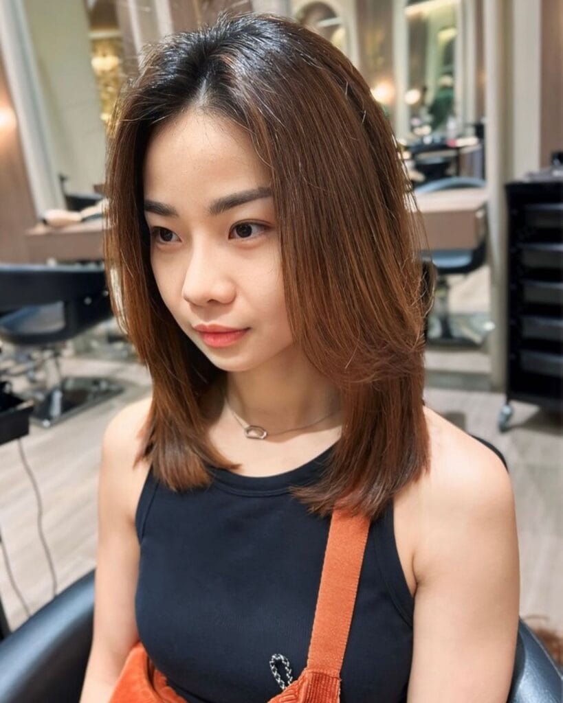 A young woman with a medium-length auburn brown haircut featuring feathered face-framing layers and a center part.