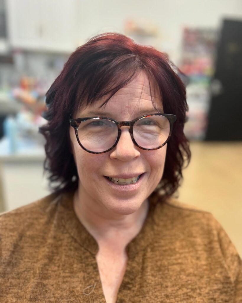 A woman with glasses wearing a textured medium-length burgundy hairstyle with choppy side-swept bangs and layered waves.