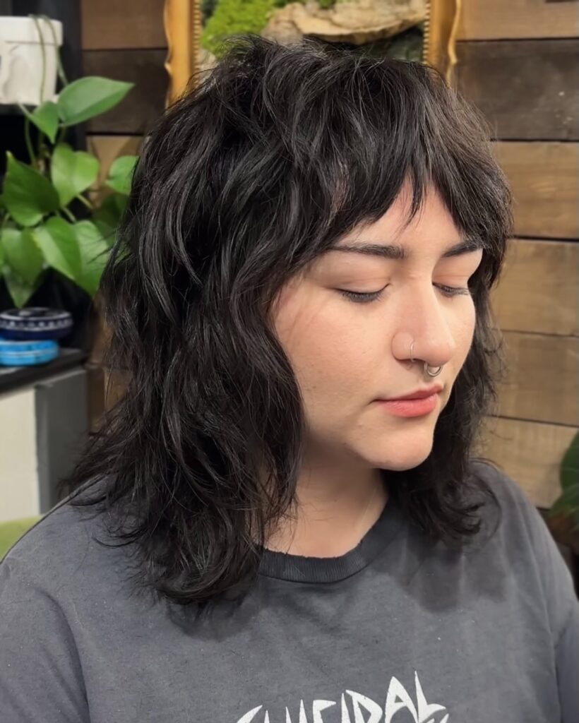 A woman with a medium-length black shag hairstyle featuring heavy layers, messy texture, and a choppy fringe.