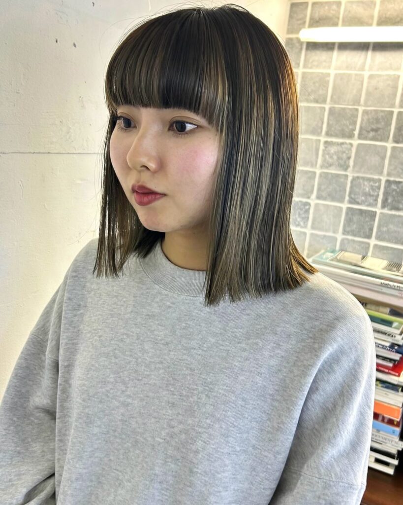 A young woman with a blunt medium-length hairstyle featuring ash-toned highlights and a thick straight-across fringe.