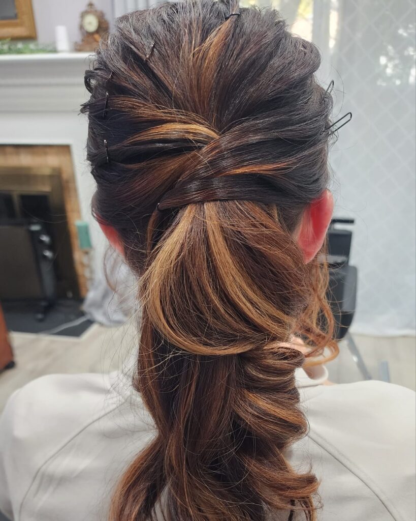 A rear view of a woman showcasing a voluminous low ponytail hairstyle featuring clever twisted sections and caramel balayage highlights on dark hair.