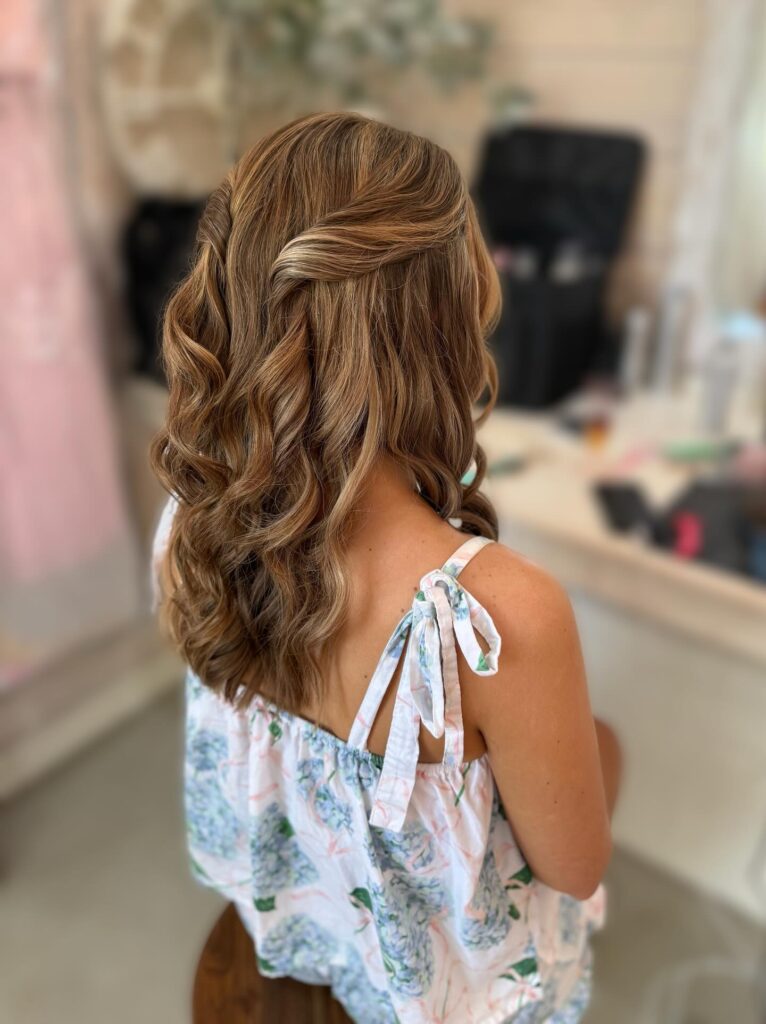 A back view of a woman with medium-length blonde hair styled in a boho half-up look with loose waves and twisted side sections.