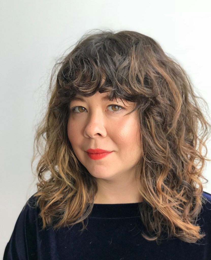 A woman with a textured wavy lob with soft fringe and subtle highlights.