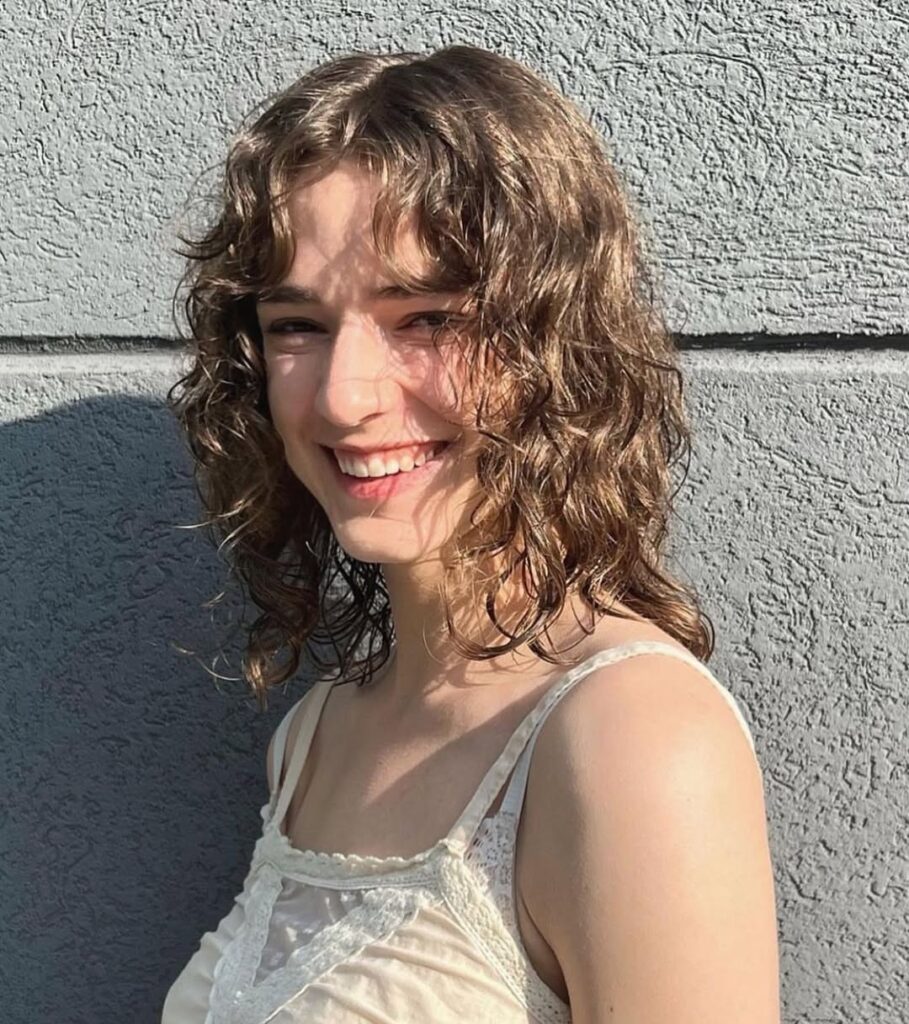 A woman with natural curly wavy hair with light bangs and soft layers.