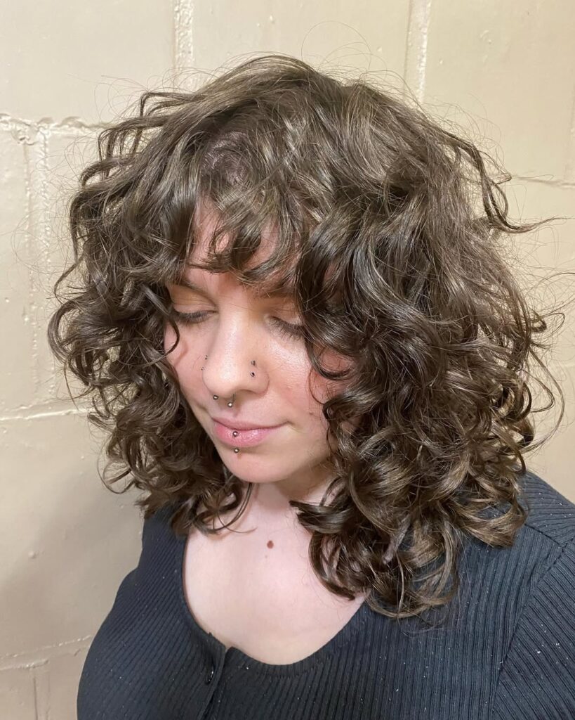 A woman with a voluminous curly shag haircut with full bangs and layered texture.