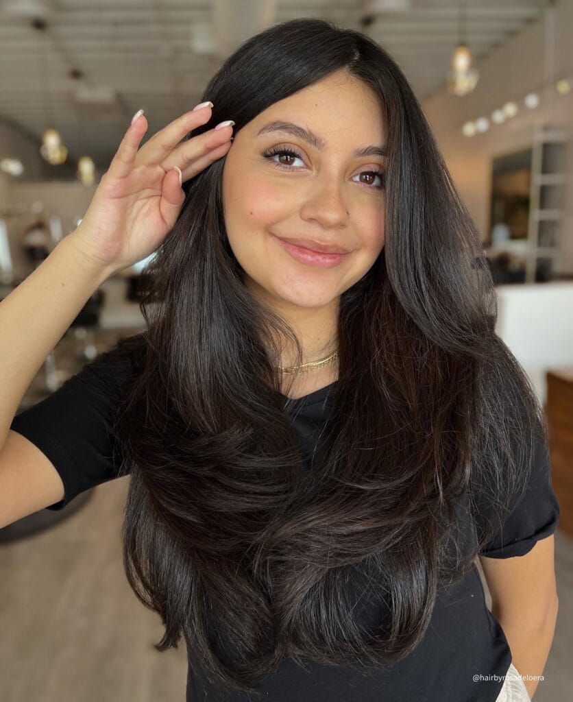 Long dark layered hair with a center part and softly curved ends for a clean polished look.