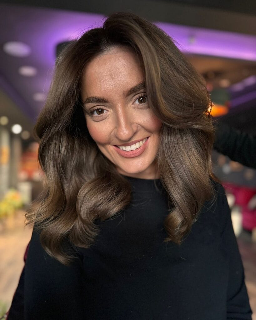 Medium length brunette hair styled in soft glam waves with a side part.