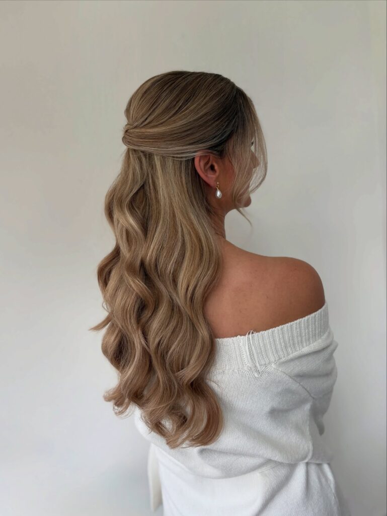 A young woman from behind showcasing a half up hairstyle with a elegant twist and long cascading blonde waves.