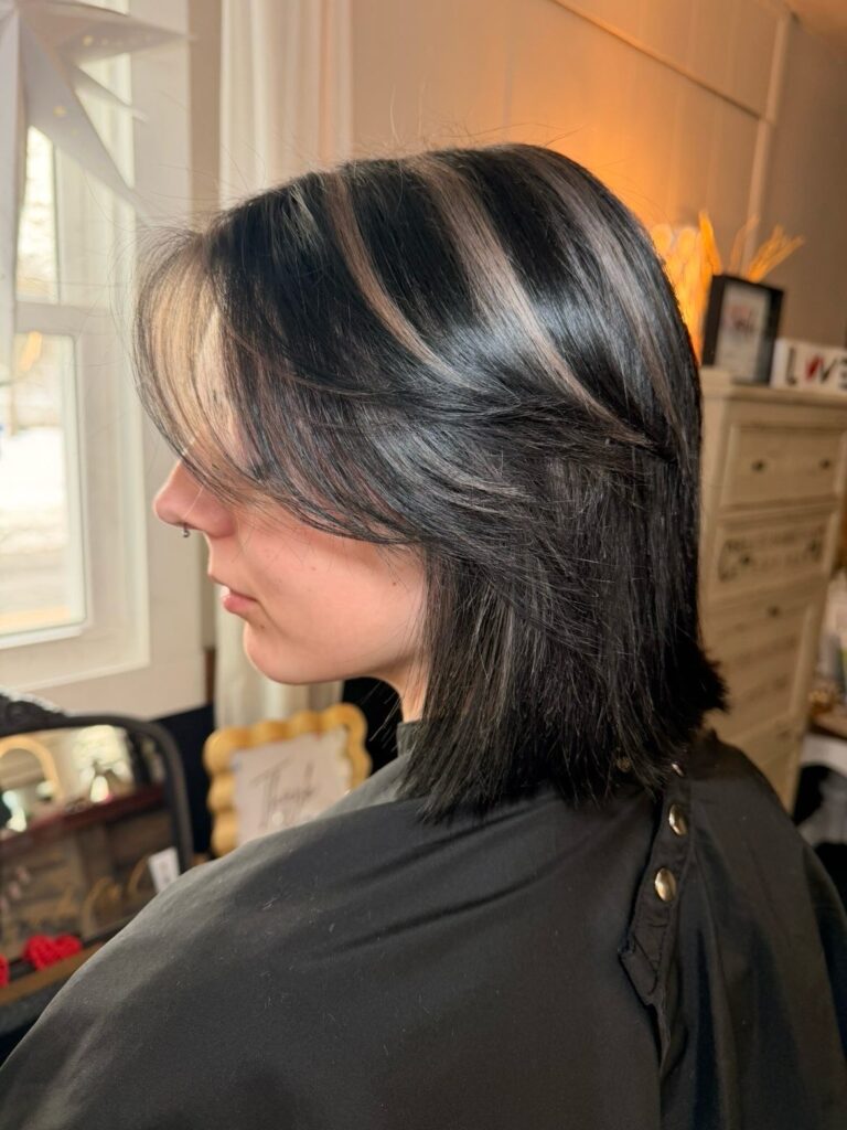 A side profile of a person with a black wolf cut hairstyle featuring ashy blonde highlights and choppy face framing layers.