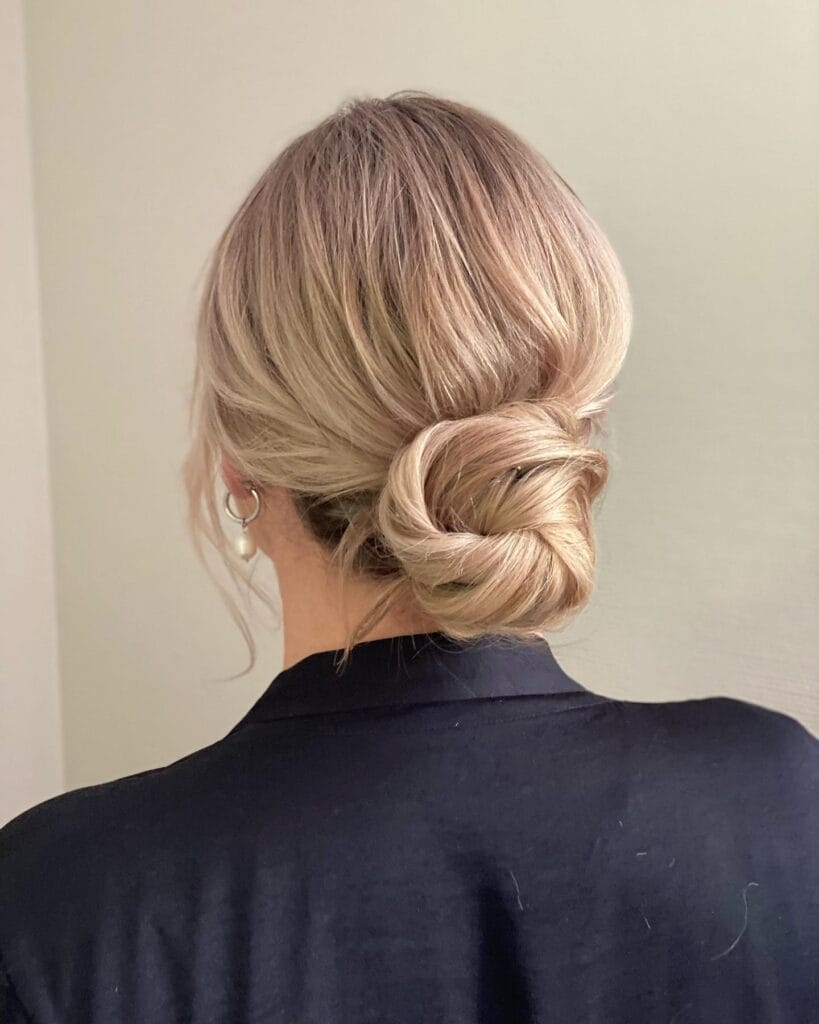 A woman with blonde hair styled in a smooth low knot at the back of the head.