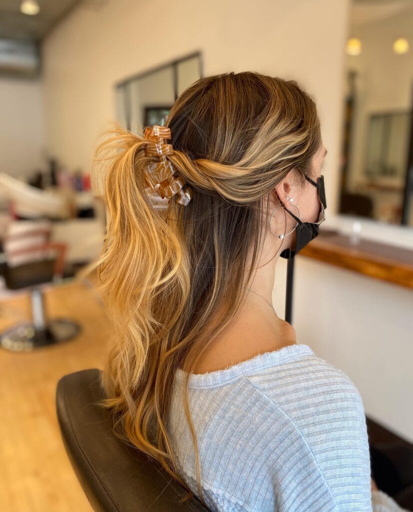A woman with long hair styled in a half up ponytail with a clip and soft waves.