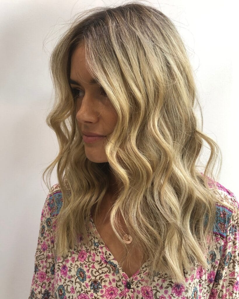 A woman with shoulder length wavy hair styled with a middle part and soft texture.