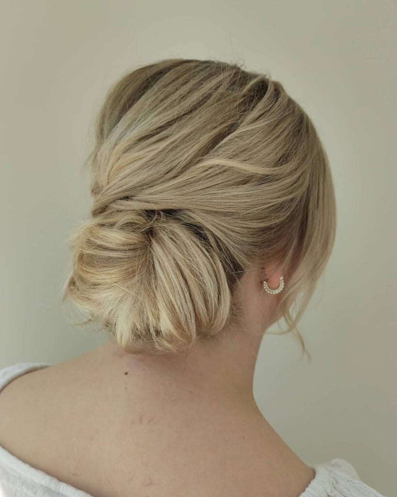 A woman with blonde hair styled in a soft twisted low bun with a relaxed finish.