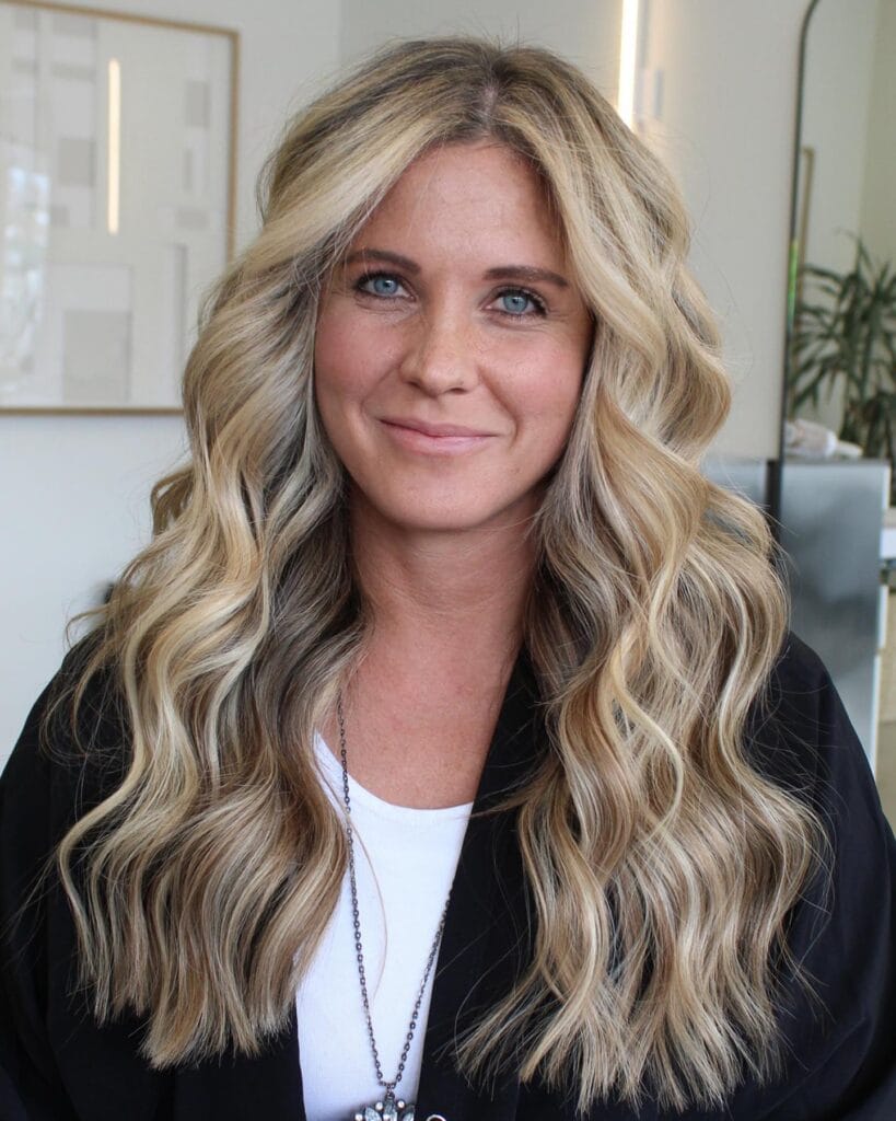 A woman with long blonde hair styled in soft loose waves with natural volume.