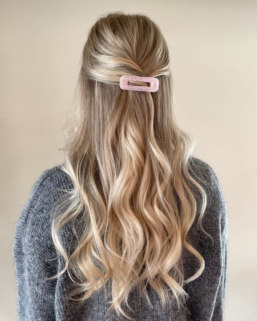 A woman with long wavy blonde hair styled in a half up look with a claw clip.