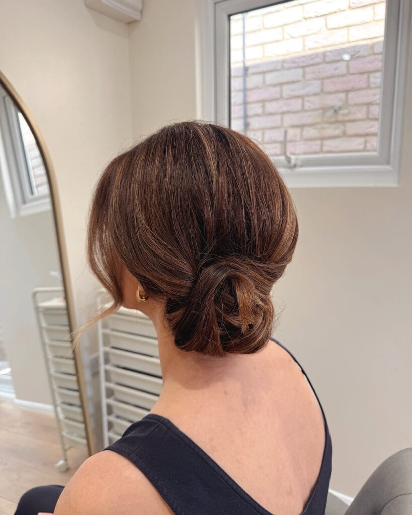 A woman with short brown hair styled in a small low bun at the nape.