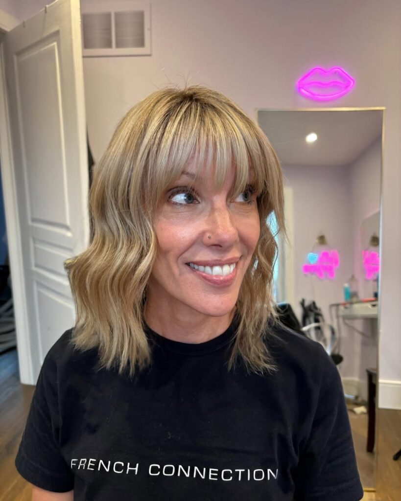 Wavy blonde bob with full soft bangs and a soft textured finish.