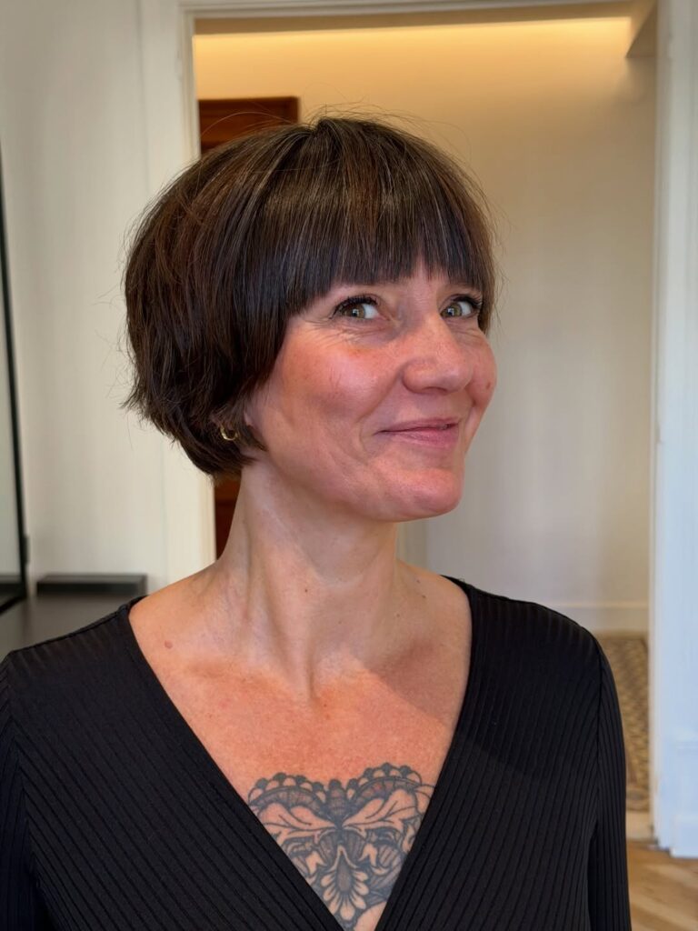 Short rounded brunette bob with full straight bangs and a smooth polished finish.