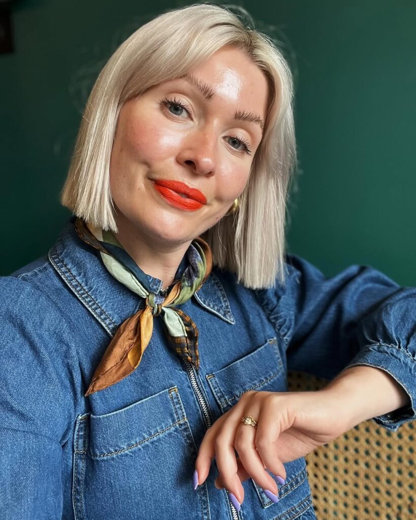 Sleek blonde blunt bob with straight bangs across the forehead.