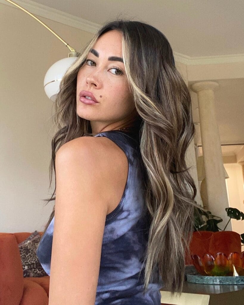 A woman with long wavy brown hair featuring bright blonde money piece highlights and voluminous layers.