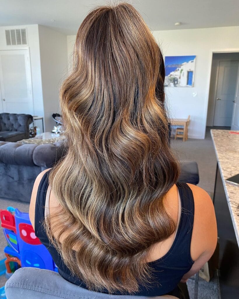 Long glossy brunette hair with defined waves and warm dimensional highlights.