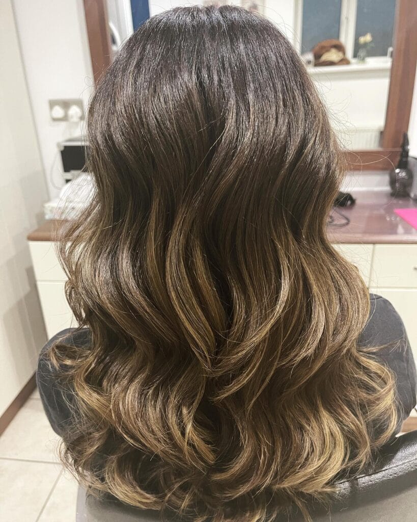Long brunette hair with soft waves and caramel highlights adding dimension.