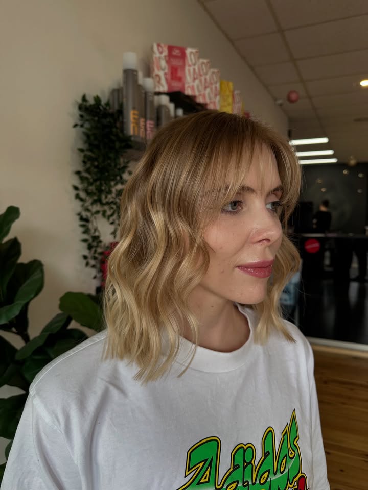 Shoulder length wavy blonde lob with soft side swept bangs and natural volume.